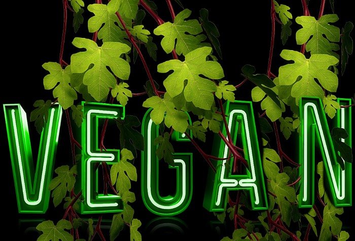 a neon sign that says VEGAN nestled in leaves.
