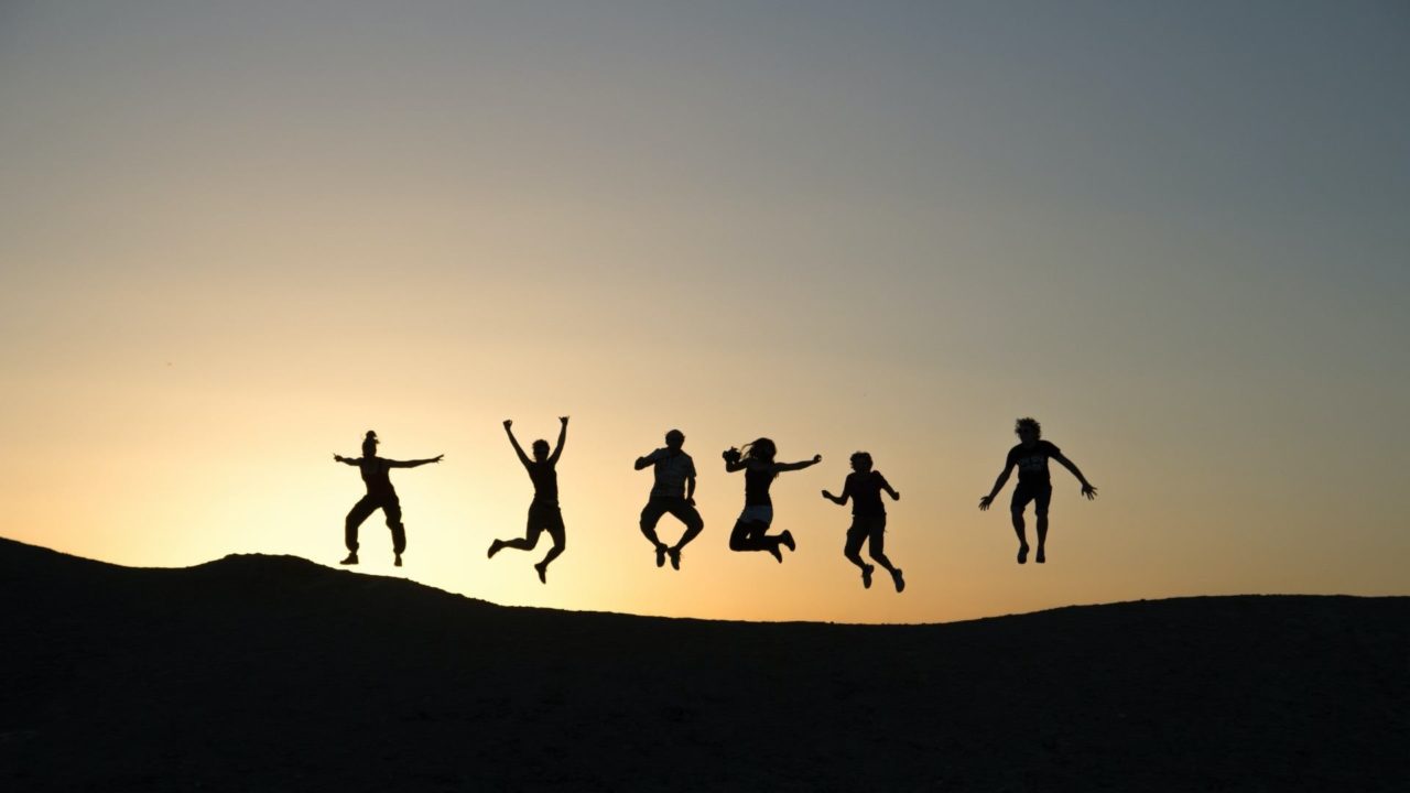 people jumping in the air with a sunset behind them.