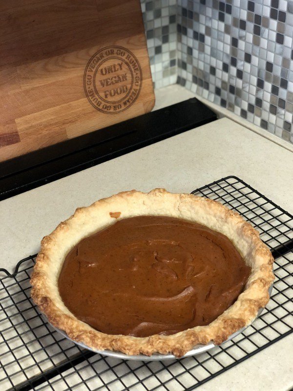 whole vegan pumpkin pie on a cooling rack with cutting board in the background.