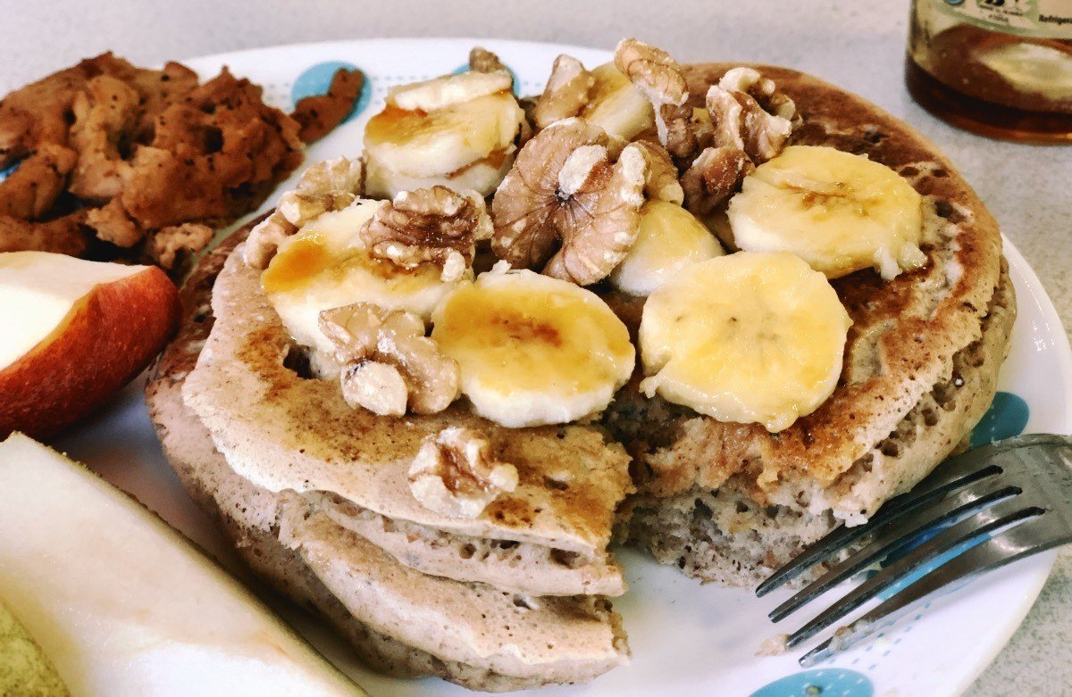 pancakes on a plate with syrup, bananas, and walnuts on top and a bite missing.