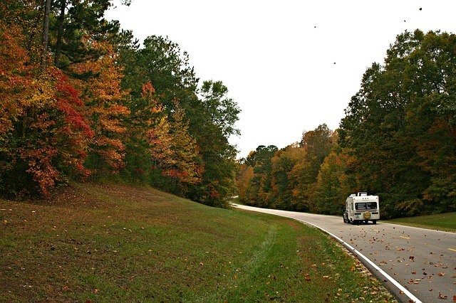 and rv on a road with fall trees alongside.