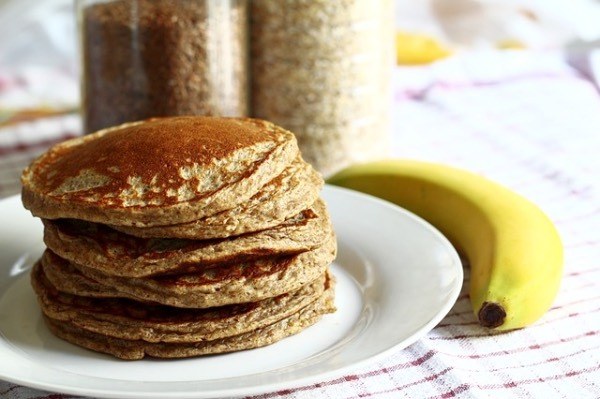 a stack of pancakes on a white plate with a banana to the side.