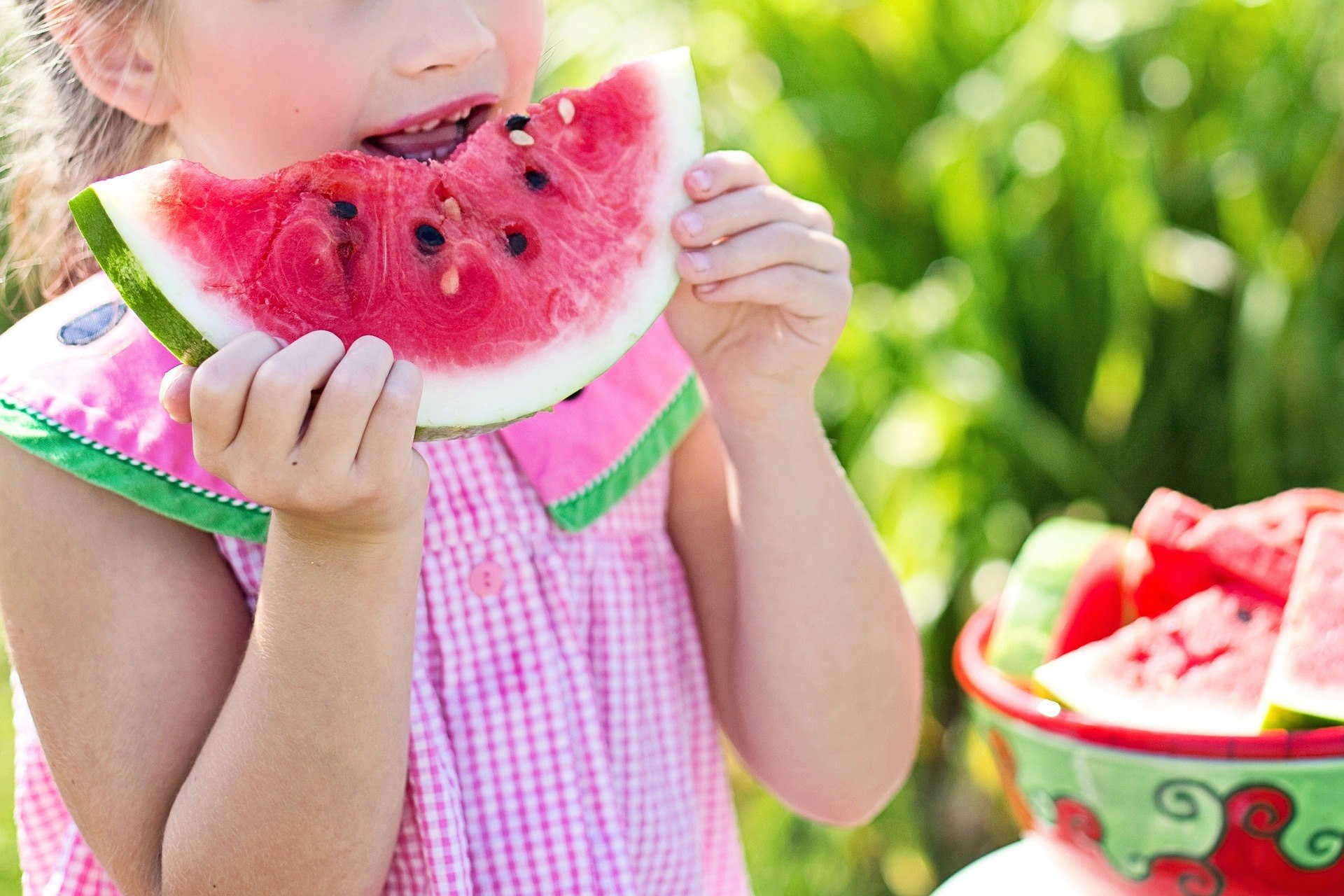 girl in a pink dress eating a watermelon slice.