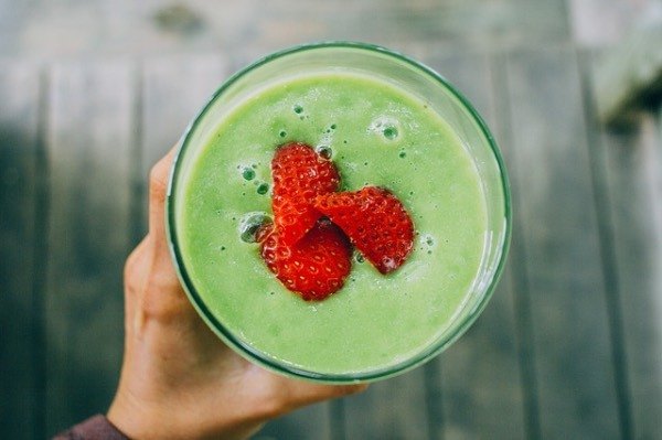 top down view of a green smoothie in a glass with strawberries on top.