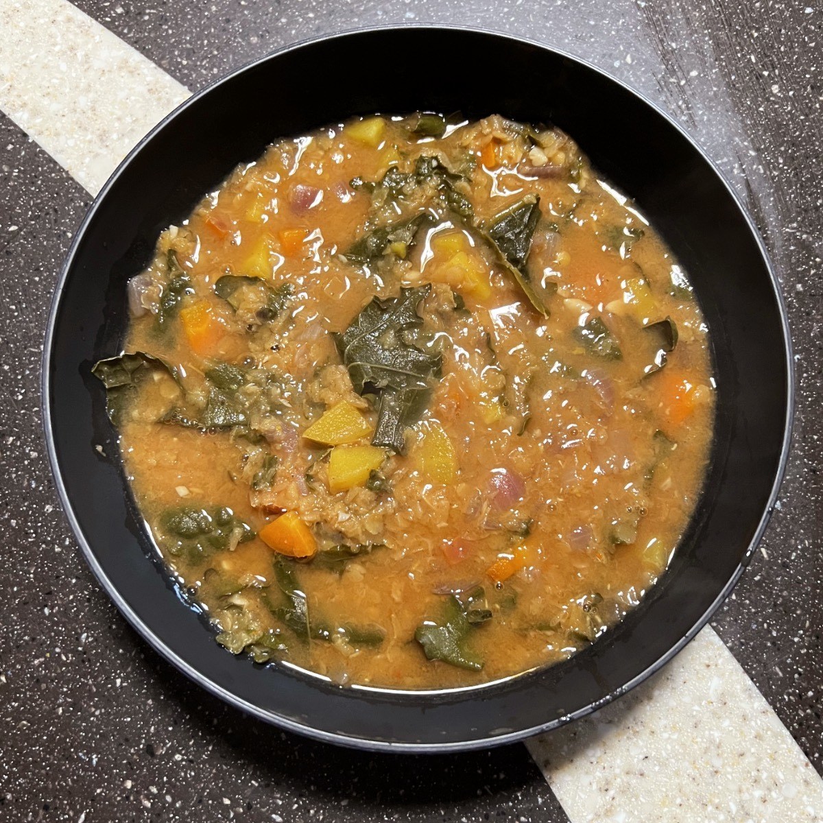 a black bowl of red lentil soup with greens.