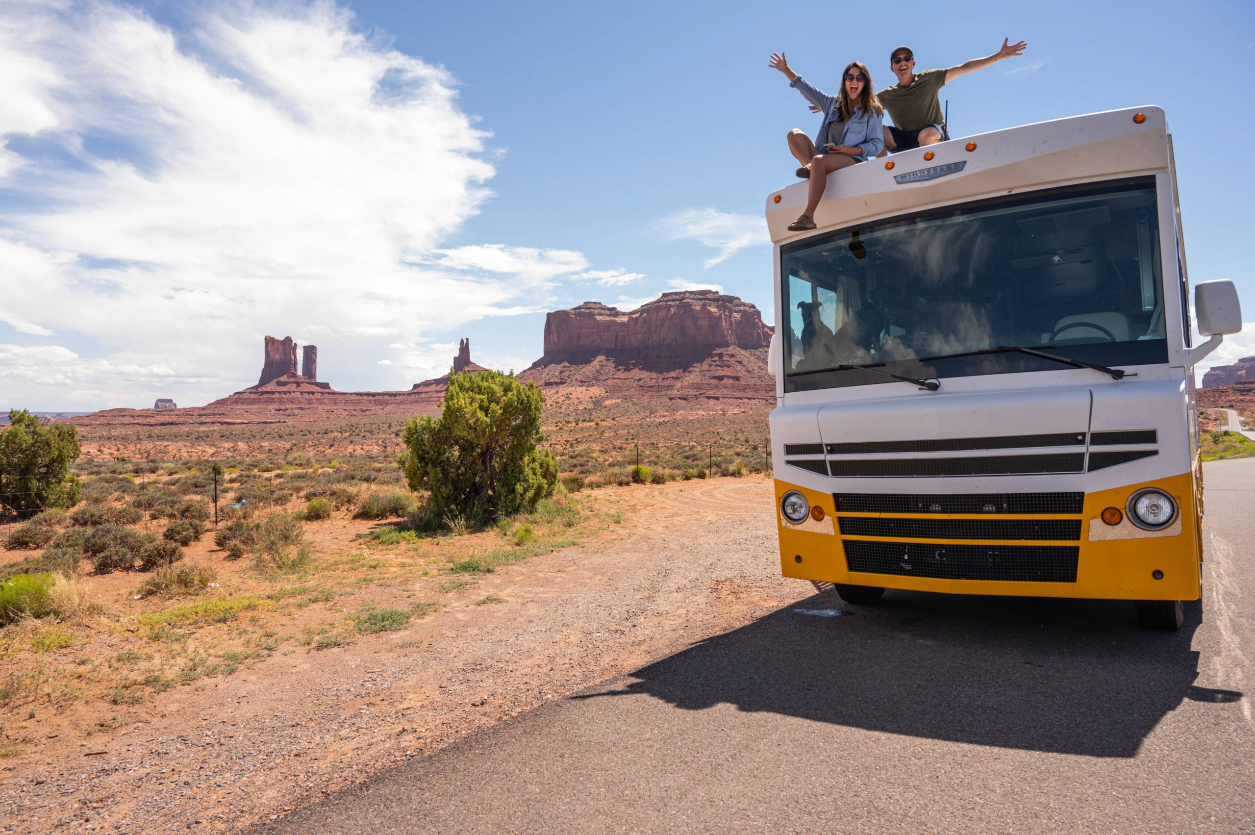 two people on top of an RV with red rocks in the background.